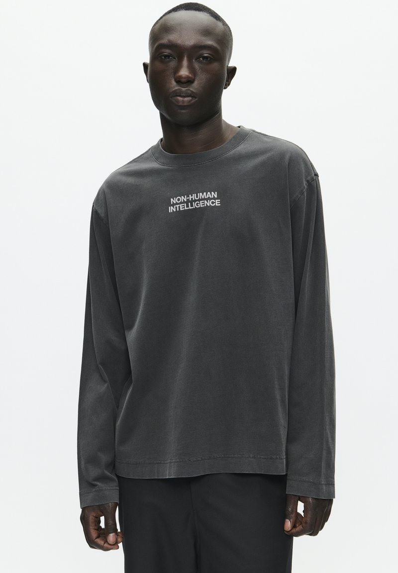 T-shirt à manches longues, gris charbon, en coton, avec le texte "INTELLIGENCE NON-HUMAINE" en blanc sur la poitrine. Design simple.