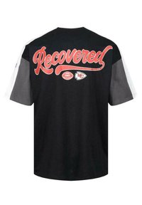 Sort t-shirt med "Recovered" i rød kursiv tekst på ryggen, med Kansas City Chiefs logoer og grå og hvide ærmer.