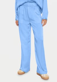 Light blue, loose-fitting pants with an elastic waistband and side pockets, made of soft fabric. Worn with beige, patterned shoes.