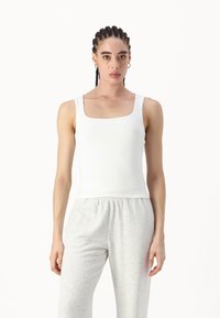 Hvit, tettsittende tank topp med kvadratisk utringning og brede stropper. Kombinert med lysegrå, løstsittende joggebukser. Glatt tekstur.