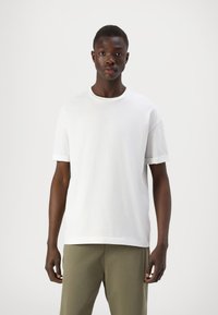 Witte katoenen T-shirt met een ronde hals en korte mouwen, met opgerolde manchetten, gecombineerd met olijfgroene broek.