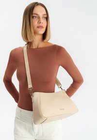 Borsa a spalla in pelle beige con texture liscia, design minimale e una sola tracolla regolabile, esposta su uno sfondo semplice.