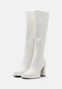 Bottes blanches montantes jusqu'aux genoux en matériau synthétique lisse, avec un bout carré et un talon épais ; dotées d'une fermeture éclair latérale et d'un design minimaliste.