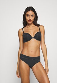 Crni grudnjak s glatkim šalicama i podesivim naramenicama, uparen s odgovarajućim crnim bikinijem s suptilnim logotipom i elastičnom waistband.