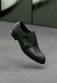 Μαύρο δερμάτινο παπούτσι με κομψό σχέδιο, διπλές αγκράφες και λείο, γυαλιστερό φινίρισμα. Διαθέτει στρογγυλή μύτη και χαμηλό τακούνι.