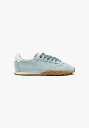 Zapatilla de ante azul claro con talón blanco, cordones azules y suela de goma color caramelo con puntos de agarre elevados.