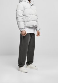 Lys grå pufferjakke med hætte og elastiske manchetter, båret over en hvid skjorte og mørkegrå bukser, parret med hvide sneakers.