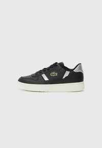 Sneaker in pelle nera con accenti argentati, suola bianca e logo ricamato verde. Presenta un design classico a bassa altezza e chiusura con lacci.
