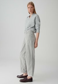 Maglione grigio chiaro in misto lana con scollo a V e maniche arrotolate, abbinato a pantaloni in velluto a coste grigio chiaro a vita alta e mocassini violacei scuri.