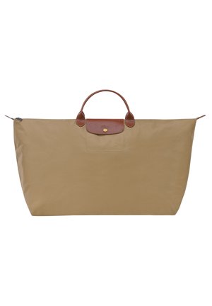 Stor beige rejsetaske med brune læderhåndtag og klap, med en guldfarvet trykknaplukning på hvid baggrund.