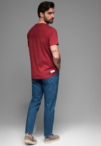 Červené tričko s krátkým rukávem a kontrastní zadní částí, kombinované s modrými džínami a šedými slip-on botami. Jednoduchý design, ležérní střih.