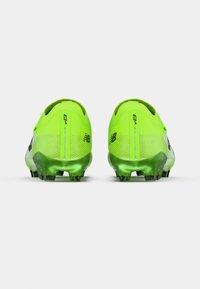 Des chaussures de football vert néon avec une tige texturée, des accents noirs et une semelle verde semi-transparente avec plusieurs crampons.
