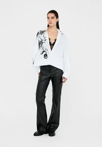 White button-up shirt with black floral design on one side, paired with black leather pants and a lace camisole, featuring relaxed fit and long sleeves.