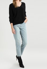 Musta neulottu V-kaula-aukkoinen villapaita pitkillä hihoilla, yhdistetty vaaleansinisiin korkeavyötäröisiin farkkuihin ja mustiin stiletto-saappaisiin. Rento asu, jossa on kontrastia tekstuurissa.