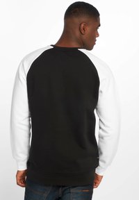 Felpa raglan bianco e nero con una texture morbida, caratterizzata da maniche a contrasto e un colletto a coste. Design semplice, vestibilità casual.