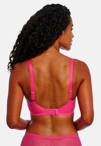 Fuchsia bh met verstelbare bandjes, geribbelde textuur en haak-en-oogsluiting. Achteraan is de accentuerende band en de gladde afwerking zichtbaar.