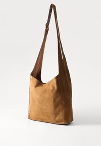 Brown suede shoulder bag with a wide, curved opening, adjustable leather strap, and a front pocket, featuring a soft texture and minimal stitching.