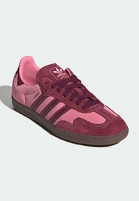 Sneaker aus Wildleder in Kastanienbraun und Rosa mit niedrigem Profil, ausgestattet mit drei dunkelrosa Streifen, strukturiertem Gummiaußensohle und markantem Zungenlabel.