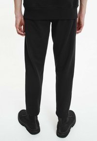 Pantaloni da jogging neri con vestibilità comoda, realizzati in tessuto morbido. Presentano una vita elasticizzata e polsini alle caviglie, abbinati a stivali neri.