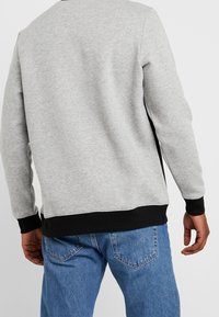 Sudadera gris con un dobladillo y puños negros acanalados, que presenta una textura suave y un diseño simple. Usada con jeans de mezclilla azules.