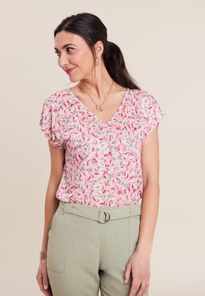 Blouse à motif floral en rose, rouge et gris. Dispose d'un col en V, de manches courtes et d'un tissu léger. Associée à un pantalon vert clair.