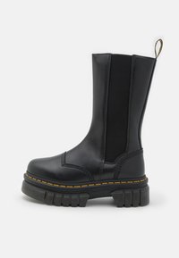 Černá kožená kotníková bota s elastickými bočními panely, masivní gumovou podrážkou, žlutými stehy a poutkem na vrchu.