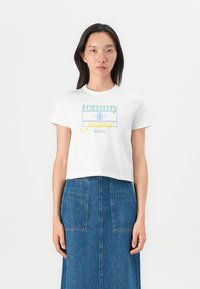 T-shirt blanc cropped avec un graphique coloré "tommy jeans", manches courtes et encolure ronde, associé à une jupe en denim.