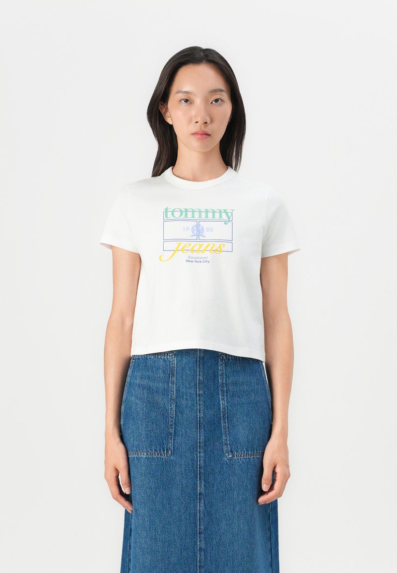 T-shirt blanc cropped avec un graphique coloré "tommy jeans", manches courtes et encolure ronde, associé à une jupe en denim.