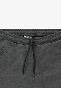Grijze joggingbroek met een elastische tailleband en een trekkoord. Twee zijzakken met rits zijn aanwezig, gemaakt van een zachte, gestructureerde stof.