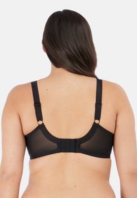 Reggiseno nero con spalline regolabili, materiale trasparente e chiusura a gancio sul retro. Presenta dettagli ondulati lungo i bordi.