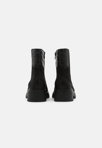 Botas negras hasta el tobillo que presentan una combinación de cuero liso y texturizado, una punta redonda y una suela gruesa con un detalle de cremallera lateral.