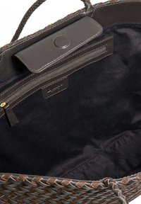 Woven brown tote bag featuring a dark leather flap and interior zip pocket. Smooth texture with contrasting stitching. Spacious design.