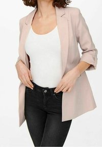 Ljusrosa blazer med en slät yta, strukturerade slag och uppvikt ärm, ihop med en vit ribbad linnetopp och svarta jeans.