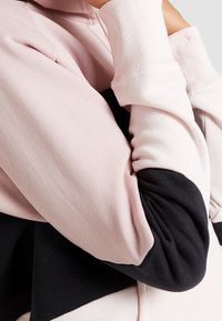 Sudadera con capucha hecha de una mezcla de telas suaves. Presenta bloques de color rosa y negro, puños acanalados y un ajuste relajado con detalles fruncidos.