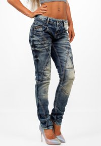 Jeans in denim azzurro chiaro con un design aderente, caratterizzati da cuciture angolate e dettagli strappati. Abbinati a tacchi alti luminosi e multicolori.