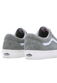 Pár šedých suédových tenisek Vans s bílými boky, bílými podrážkami a logy "Vans Off The Wall" na zadních patách, z pohledu zezadu.
