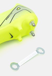 Yellow Nike football boot with textured mesh upper, black accents, and detachable metallic studs, accompanied by a silver maintenance tool.