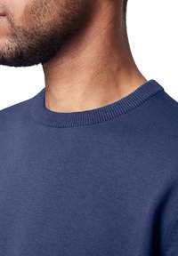 Dunkelblaues Rundhals-Sweatshirt mit ribbeltem Ausschnitt. Weicher Strickstoff mit glatter Oberfläche, der eine Nahaufnahme des Kragens und des Schulterbereichs zeigt.