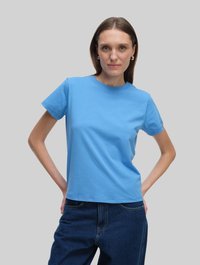 Niebieska bawełniana koszulka z okrągłym dekoltem i krótkimi rękawami, zestawiona z ciemnymi dżinsami. Materiał jest gładki i ma luźny krój.