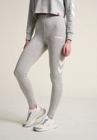 Grå leggings i mjuk tyg med slät textur, med en vit logotyp, sidomönster i chevron och resårmidja.