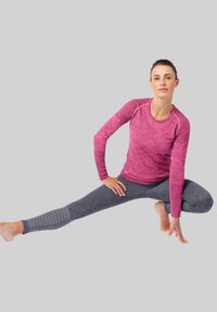 Sportoutfit met een gestructureerde roze lange mouwen top en donkergrijze fitted leggings met een ribbelpatroon. Model poseert in een split.