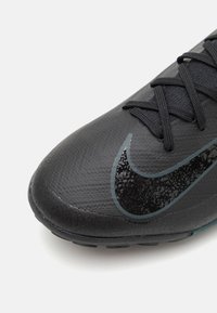 Black athletic shoe with a textured synthetic upper, featuring a prominent black Nike swoosh and dark rubber outsole. Laces are black.
