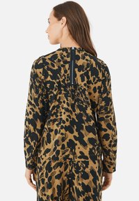 Dyreprintet bluse i brun og sort, med lange ærmer, lynlåslukning i ryggen og samlet detaljer ved skuldrene.