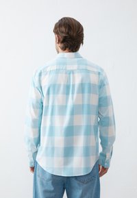 Hellblau und weiß karierter Langarmshirt mit Knopfmanschetten und abgerundetem Saum, aus weichem Stoff, von hinten betrachtet.