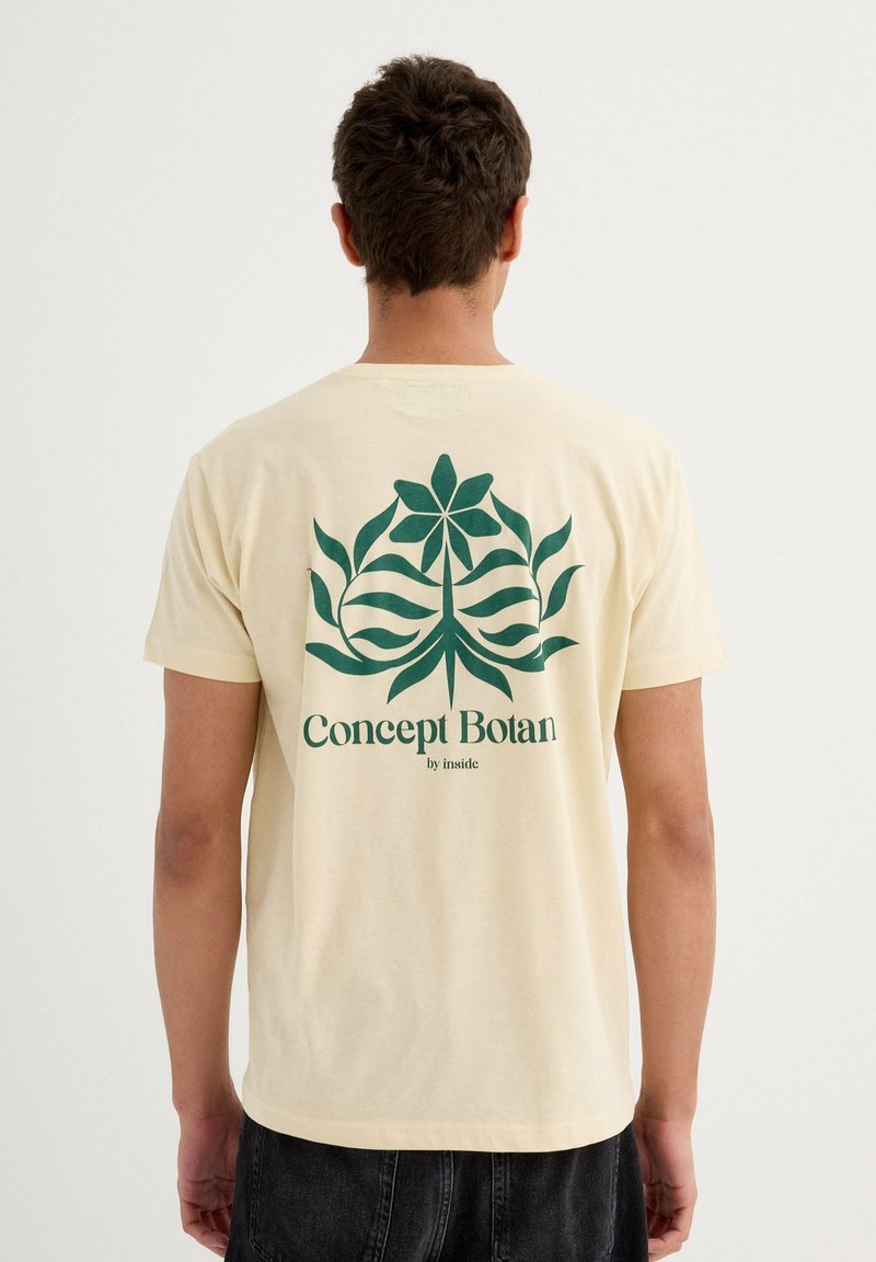 Camiseta de algodón beige con un estampado botánico verde en la parte posterior, que presenta flores y hojas estilizadas, y texto que dice "Concept Botan by inside."