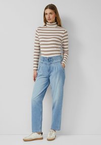 Bluzka z długim rękawem w paski, z golfem w kolorach kremowym, brązowym i burgundowym; jasnoniebieskie plisowane jeansy; białe trampki z beżowymi akcentami.