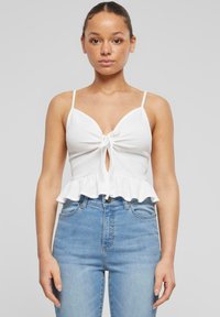 Valkoinen ribbineuleinen crop-top, jossa on solmittava etuosa ja lievänä levenevä helma. Ohuet olkaimet ja avaus avainaukolla lisäävät yksityiskohtia. Yhdistetty vaaleansinisiin korkeavyötäröisiin farkkuihin.