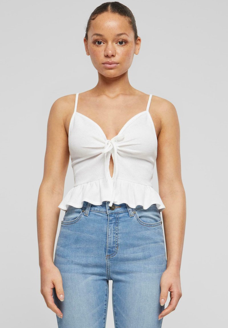 Valkoinen ribbineuleinen crop-top, jossa on solmittava etuosa ja lievänä levenevä helma. Ohuet olkaimet ja avaus avainaukolla lisäävät yksityiskohtia. Yhdistetty vaaleansinisiin korkeavyötäröisiin farkkuihin.