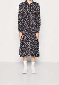 Abito lungo a maniche lunghe con stampa floreale navy, spacchettato con bottoni, colletto e falda svasata; abbinato a sneakers bianche e calzini alla caviglia coordinati.