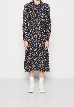 Langes Kleid mit navyblauem Blumenmuster, Knopfleiste, Kragen und ausgestellt Rock; kombiniert mit weißen Sneakern und passenden Crew-Socken.
